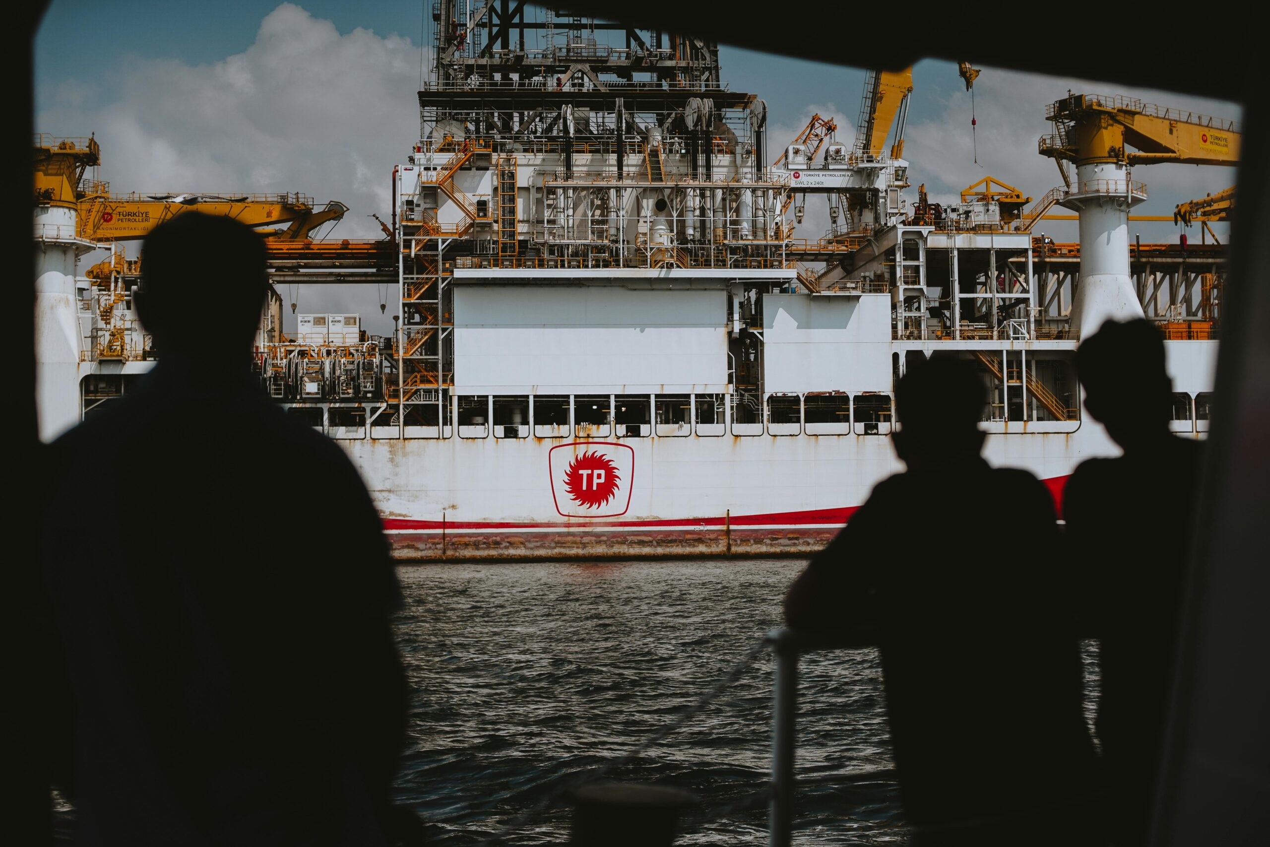Silhouetted figures observing a large offshore oil rig at sea, emphasizing maritime industry.